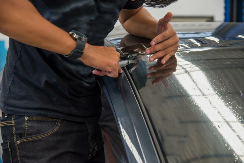 Man working on fixing window tint on a car