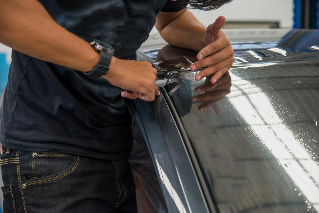 Man carefully removing window tint from a car windscreen